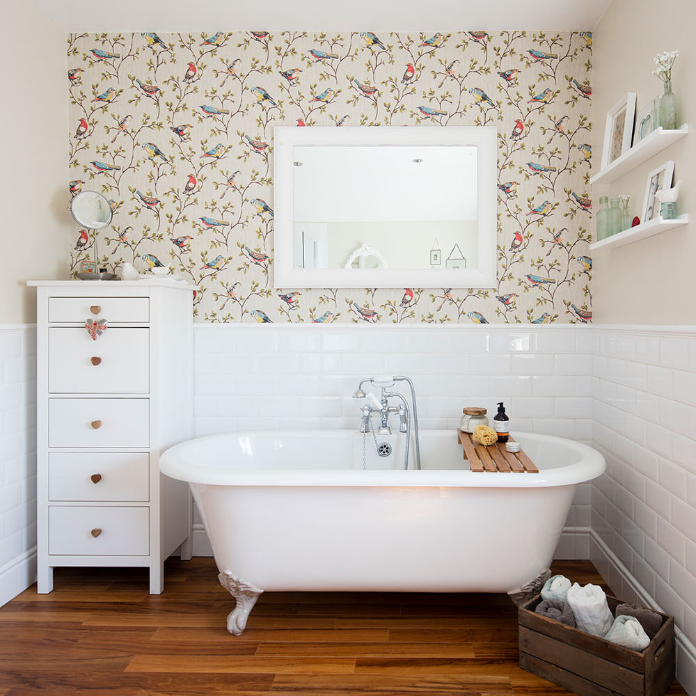 دکوراسیون حمام زیبا با کفپوش چوبی و کاشی و وان سفید که دیوار تاکیدی کاغذ دیواری شده با طرح پرنده و درختان دارد